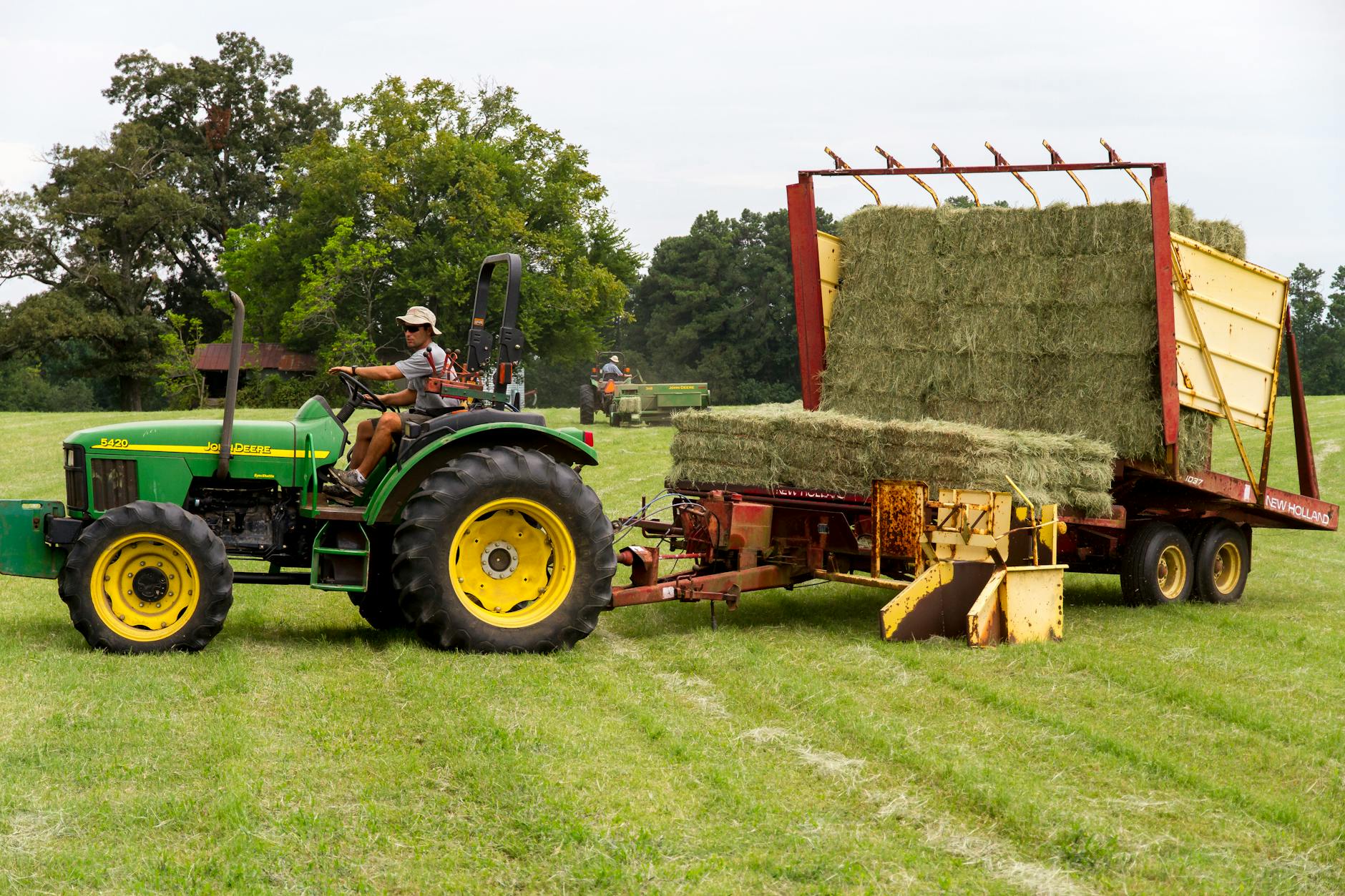man riding on riding mower carrying hays in the middle of field