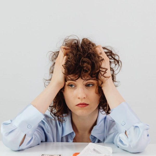 woman in blue long sleeve shirt holding her head